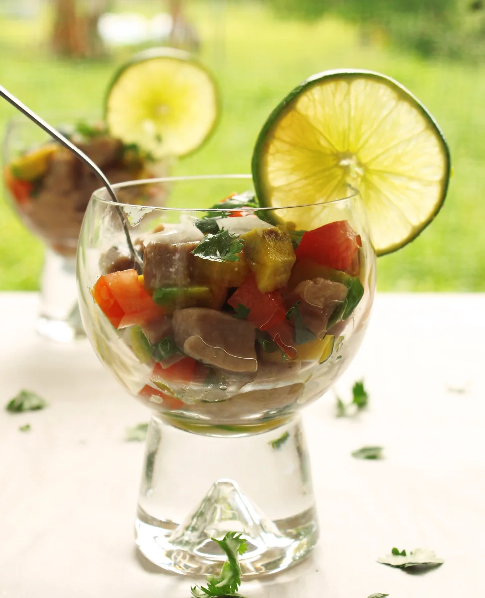 Tuna ceviche in a glass with tomato, avocado, cilantro, and a lime wheel
