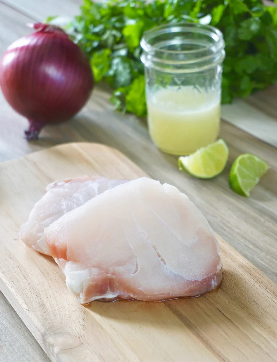 Fresh white fish fillets on a cutting board with red onion, cilantro and fresh lime juice