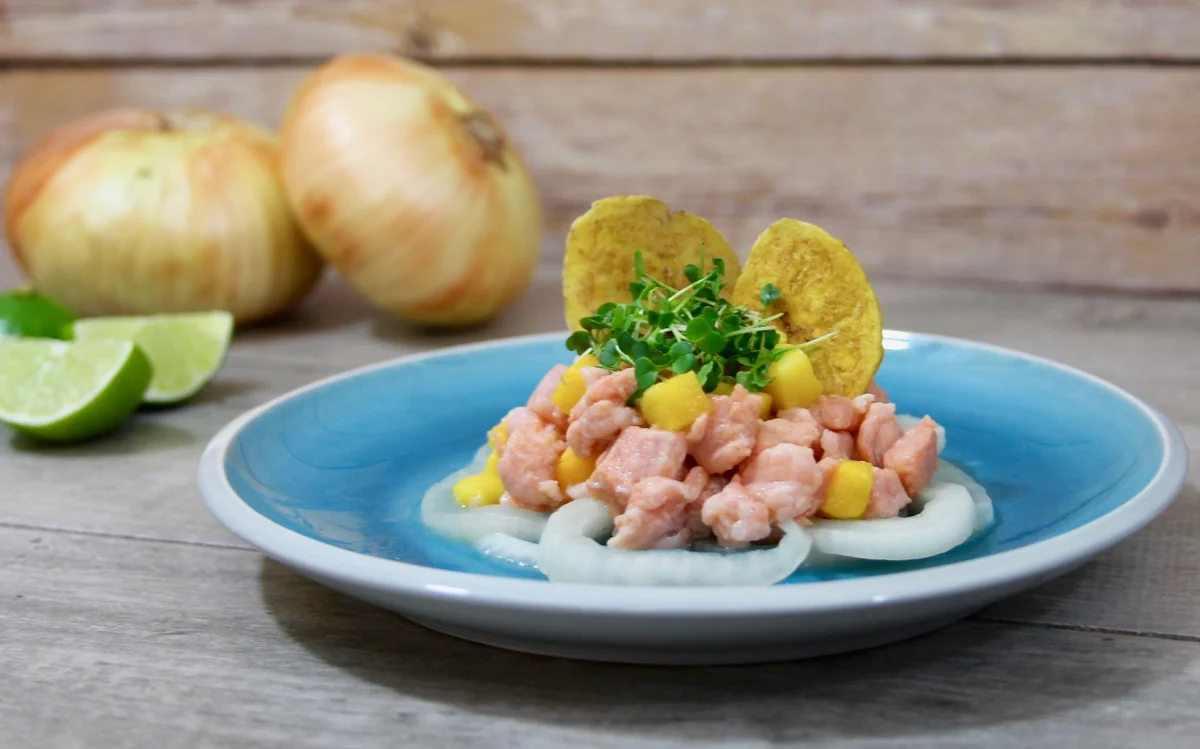 Salmon and mango ceviche on a blue plate with onion rings, microgreens and plantain chips