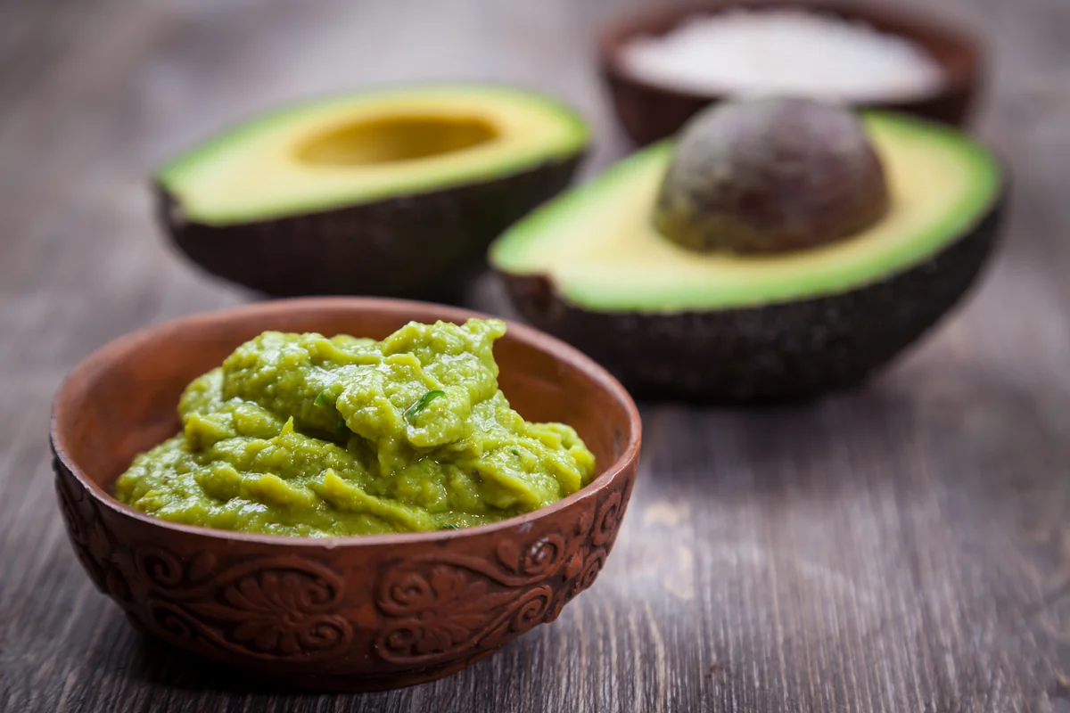 Bowl of fresh guacamole beside halved Hass avocados, the spread for Guatemalan guacamol tostadas