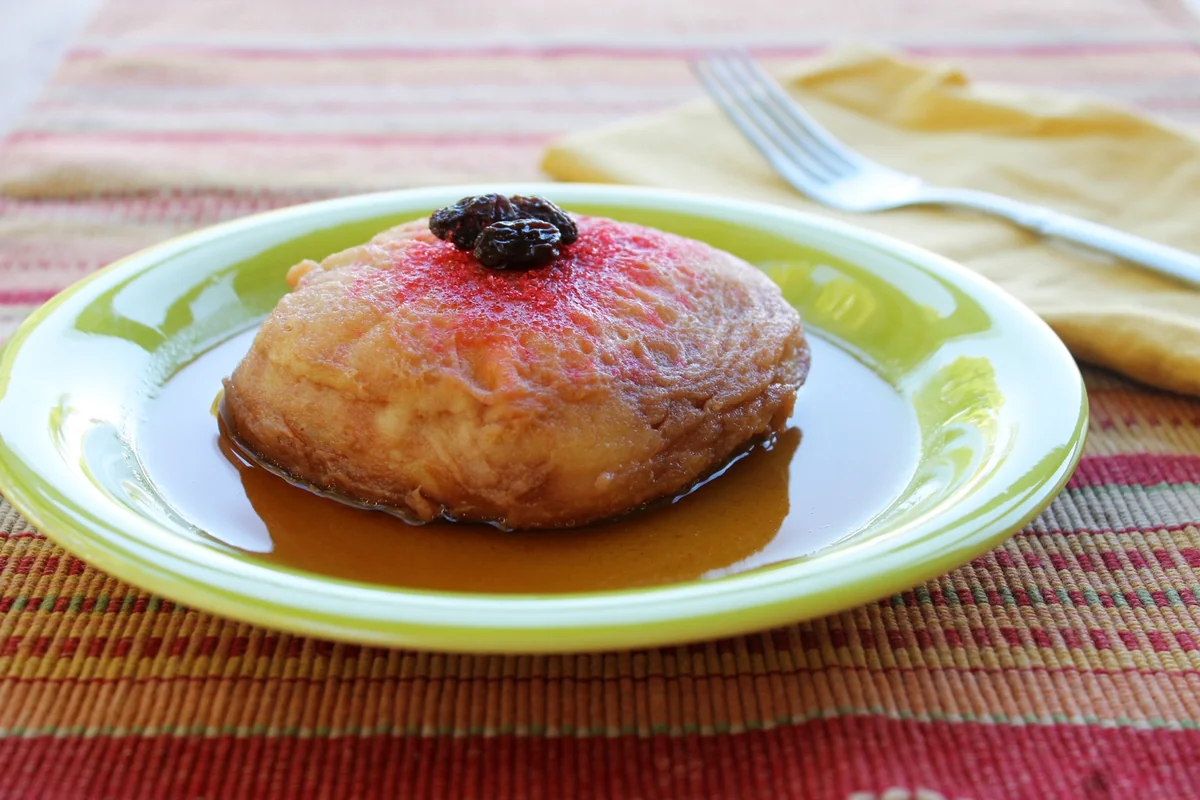 Guatemalan torreja soaked in cinnamon syrup and topped with a raisin, served on a green plate