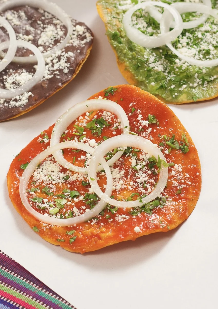 Guatemalan tostada topped with red recado sauce, onion rings, cilantro, and crumbled queso duro