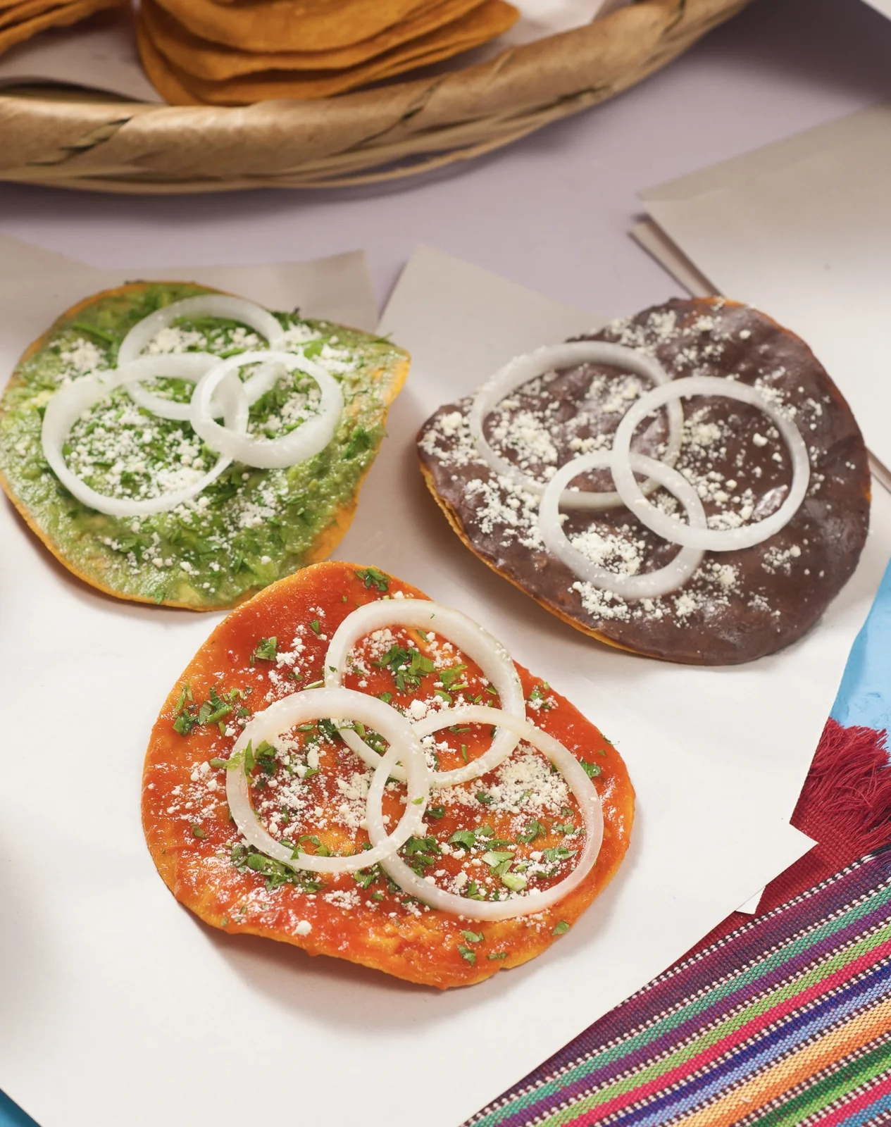 Three Guatemalan tostadas topped with guacamole, black beans, and recado salsa, garnished with onion and queso duro