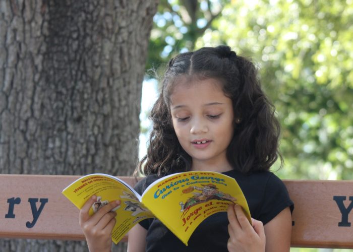 girl reading bilingual Curious George book