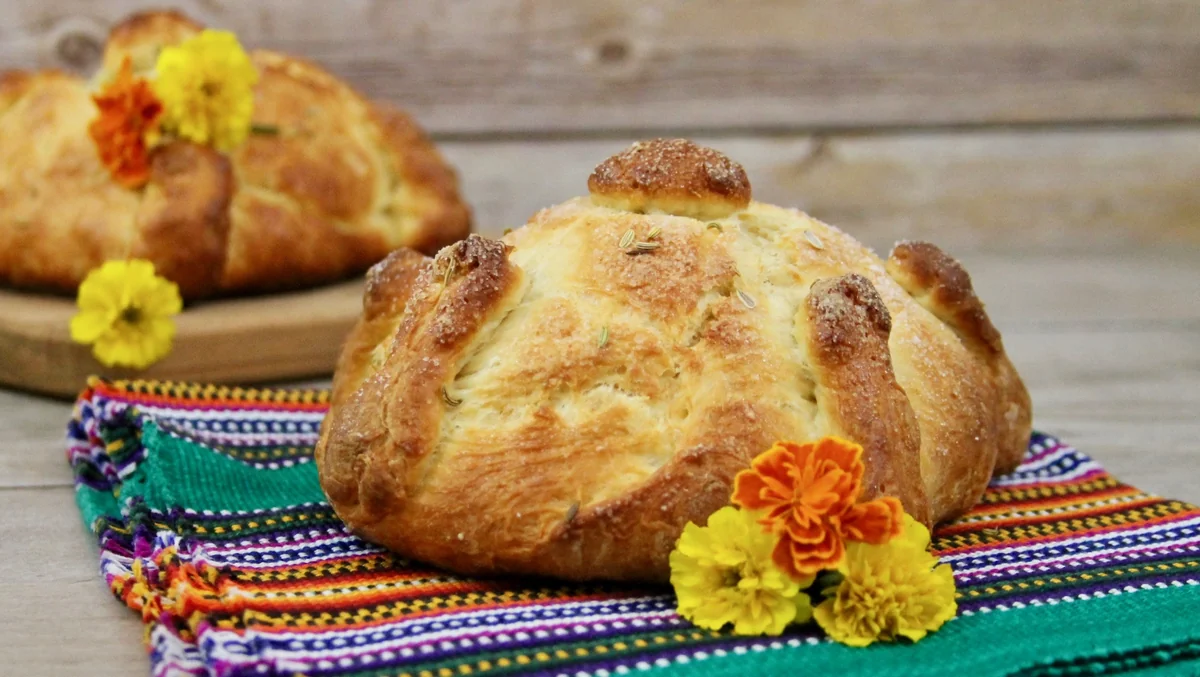 Pan de muerto loaf decorated with marigold flowers on a Guatemalan textile