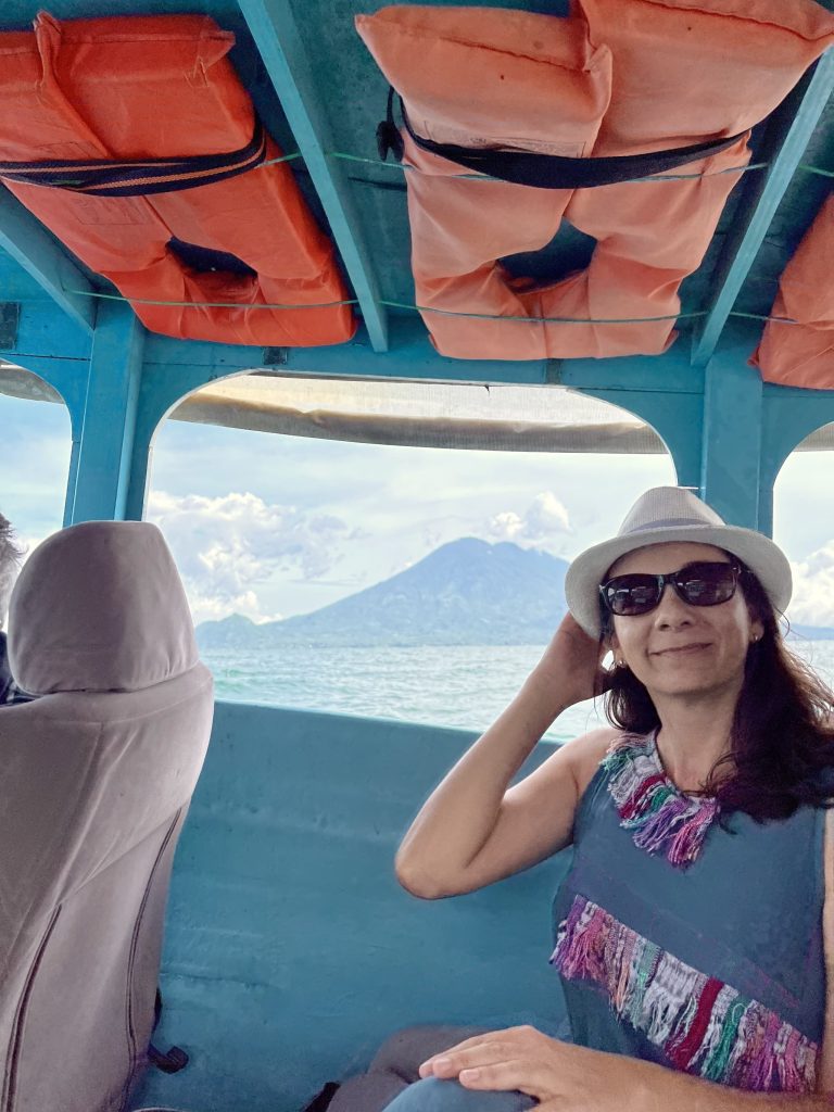 Woman in blue dress and straw hat riding a traditional boat on Lake Atitlán in Guatemala with volcano views in the background
