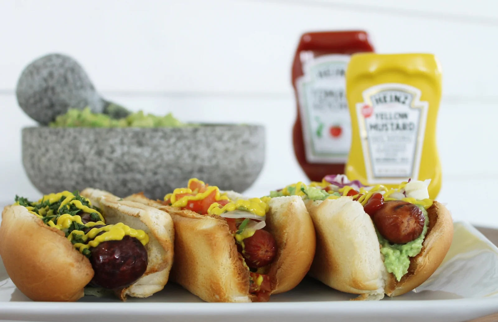 Three Guatemalan shucos on a plate topped with guacamol, cabbage, sausage, mustard, and ketchup