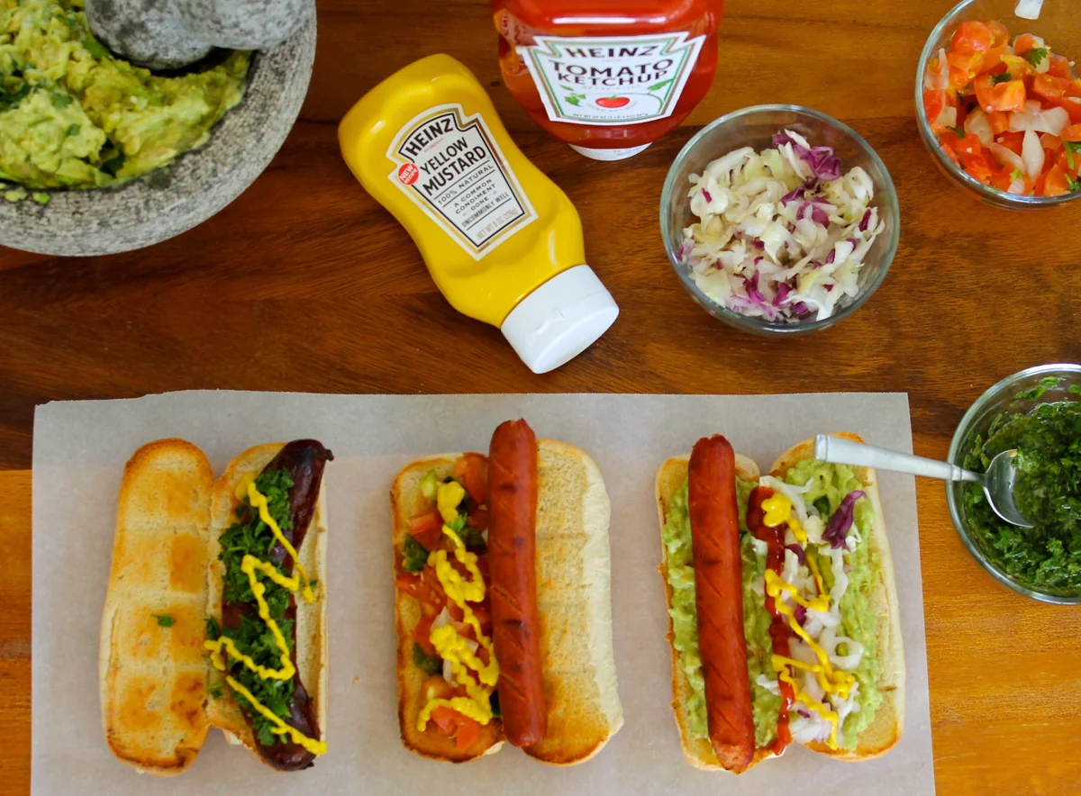 Three assembled Guatemalan shucos with longaniza, chorizo, and hot dog on toasted buns