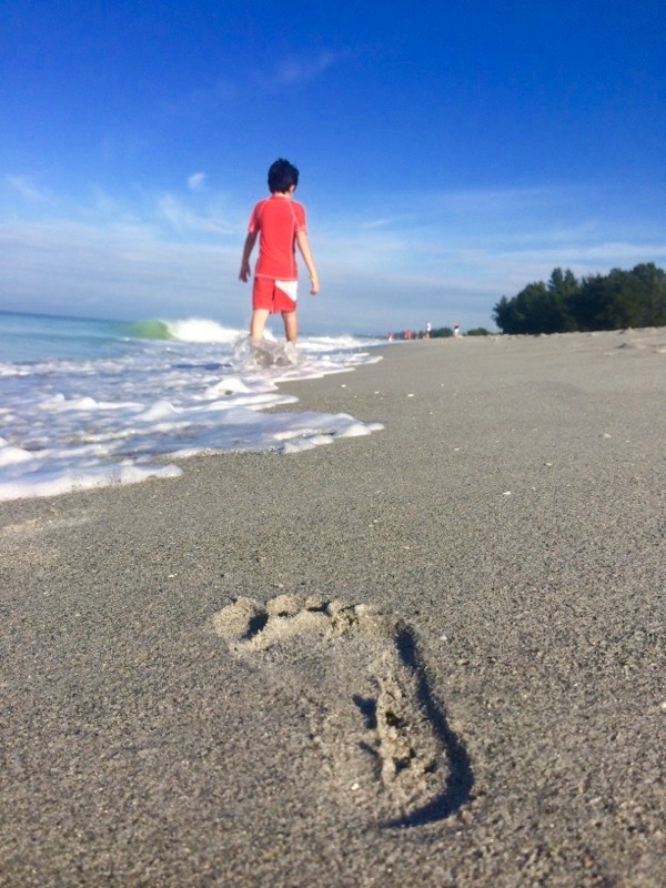 footprint on the beach with boy in the background