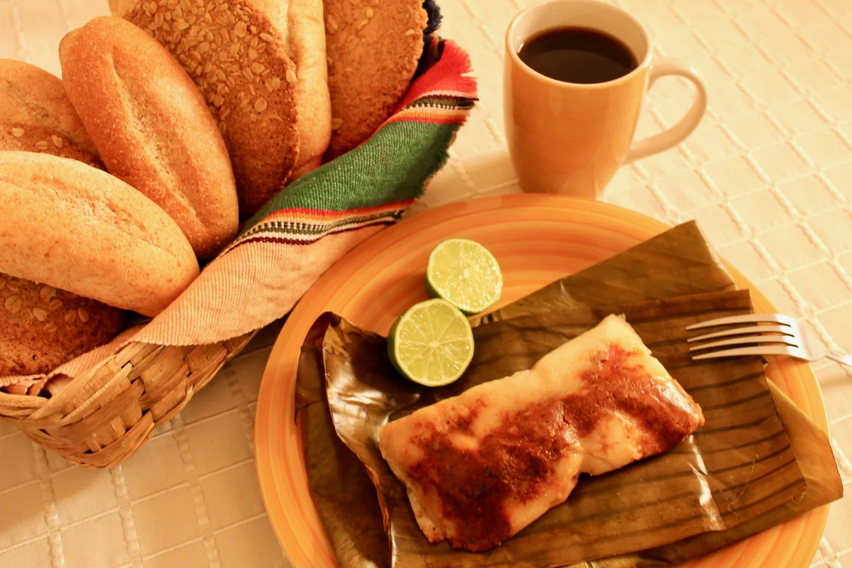 Tamal colorado guatemalteco en hoja de plátano, servido con pan y café