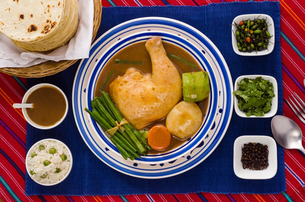 Pepián de pollo guatemalteco servido con arroz, tortillas y chiltepes