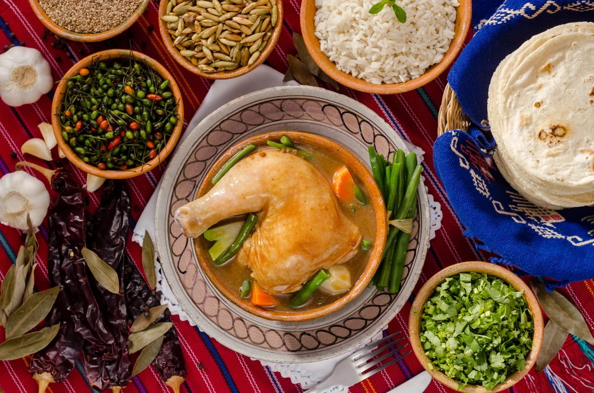 Pepián guatemalteco en olla de barro rodeado de chiles secos y ajo