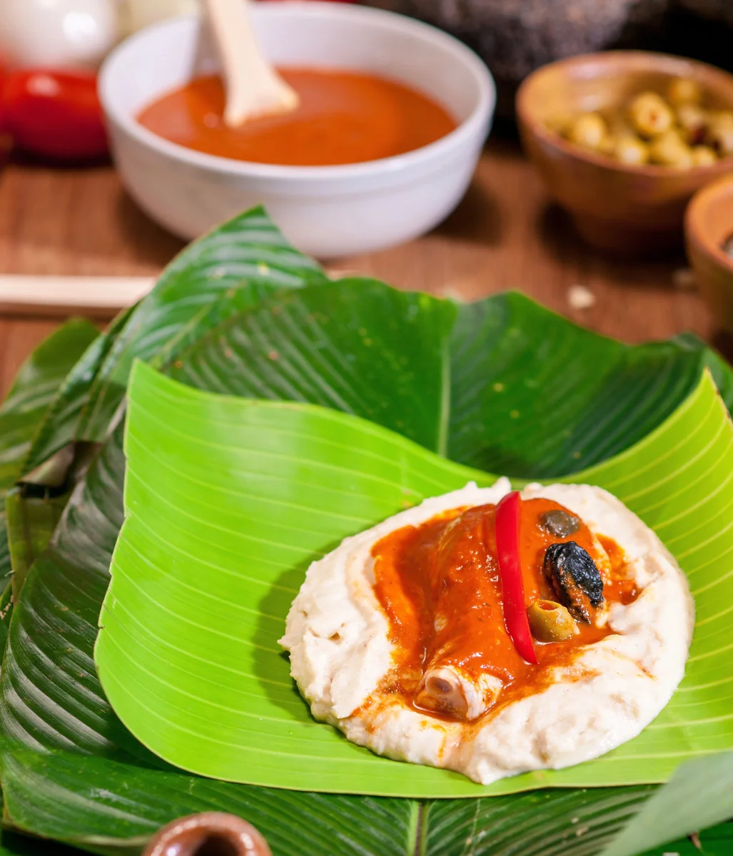 Masa sobre hoja de banano con pollo, recado rojo, chile pimiento, aceituna, ciruela pasa y alcaparras