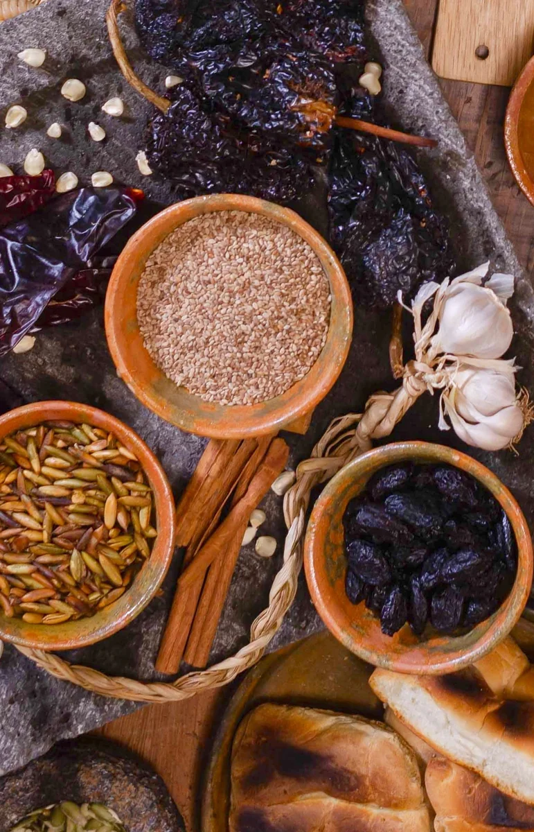 Ajonjolí, semillas tostadas y ciruelas pasas en tazones, con chiles secos, canela, ajo y pan sobre una piedra