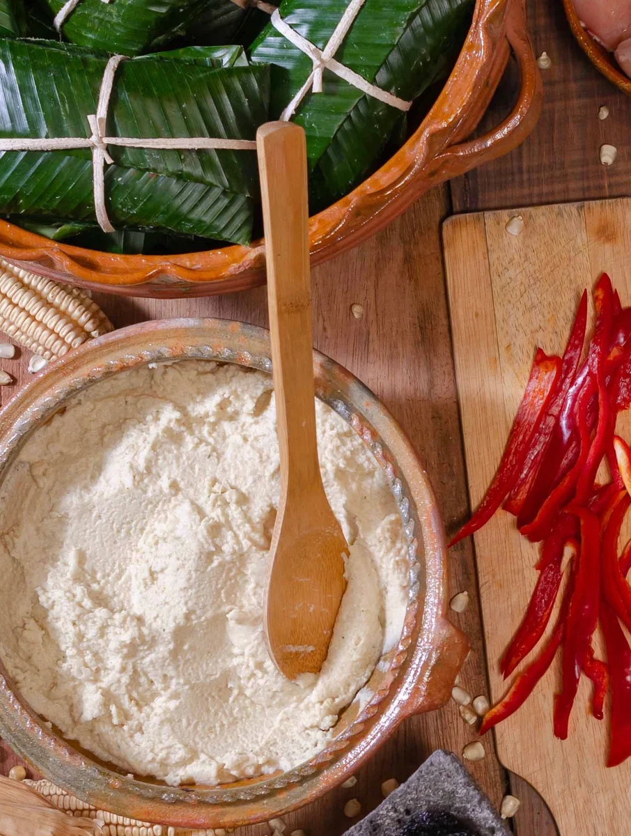 Masa para tamales hecha en casa en una olla de barro, junto a tamales en hoja de banano y chile pimiento en tiras