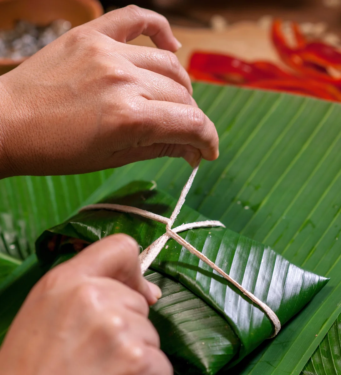 Manos anudando la cuerda alrededor de un tamal doblado en hoja de banano