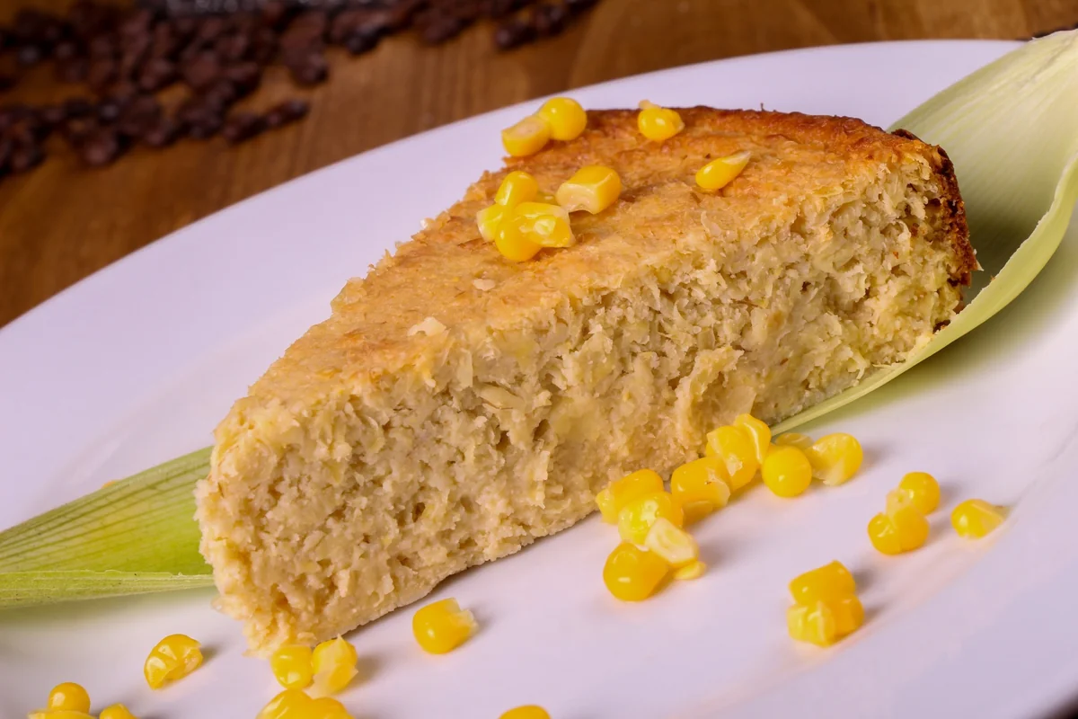 Guatemalan pastel de elote, a slice of sweet corn cake served on a corn husk with fresh kernels