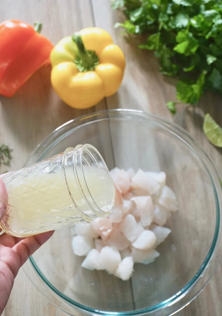 Pouring fresh lime juice over cubed white fish in a glass bowl to make Peruvian ceviche