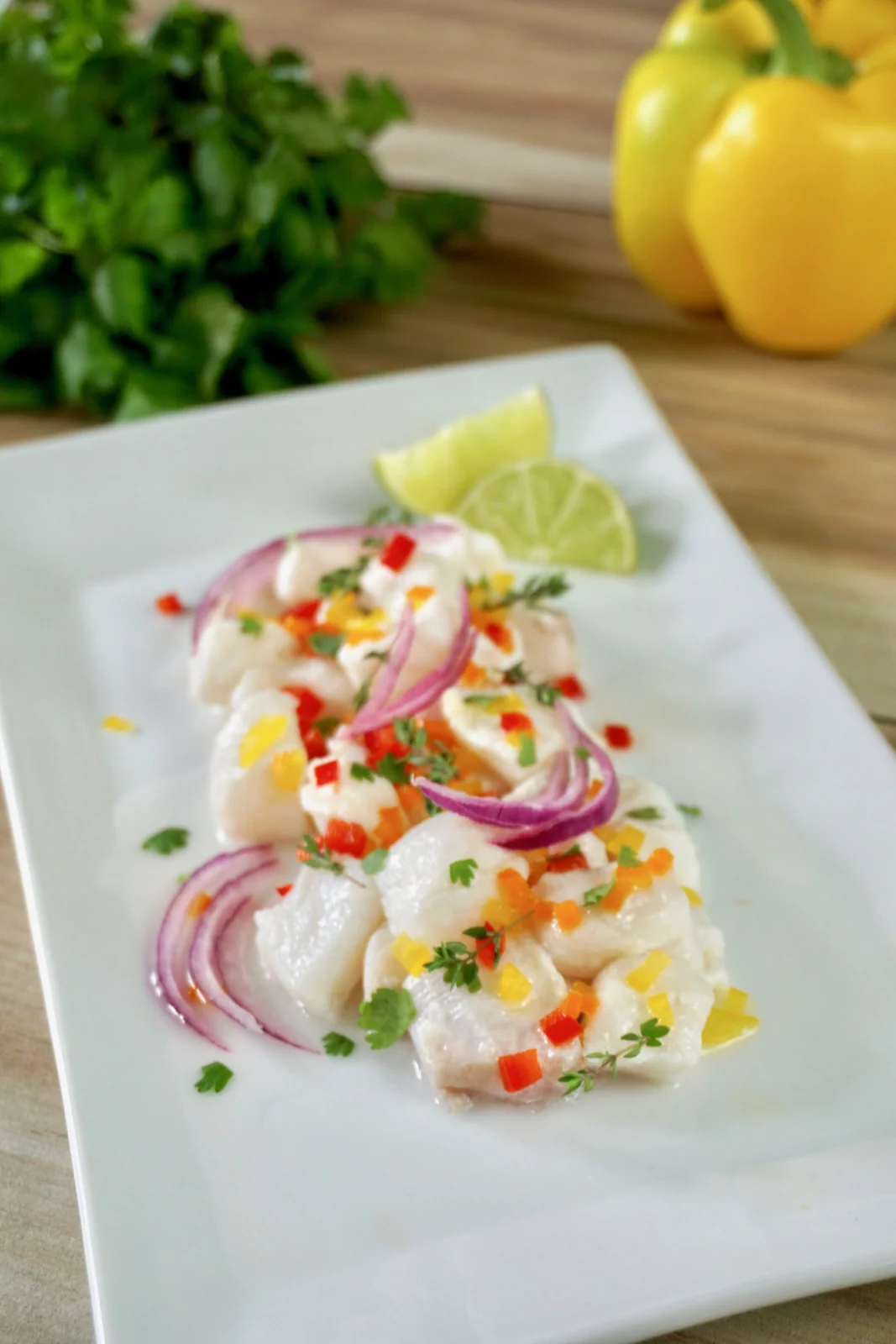Peruvian fish ceviche on a white plate with red onion, sweet peppers, and lime