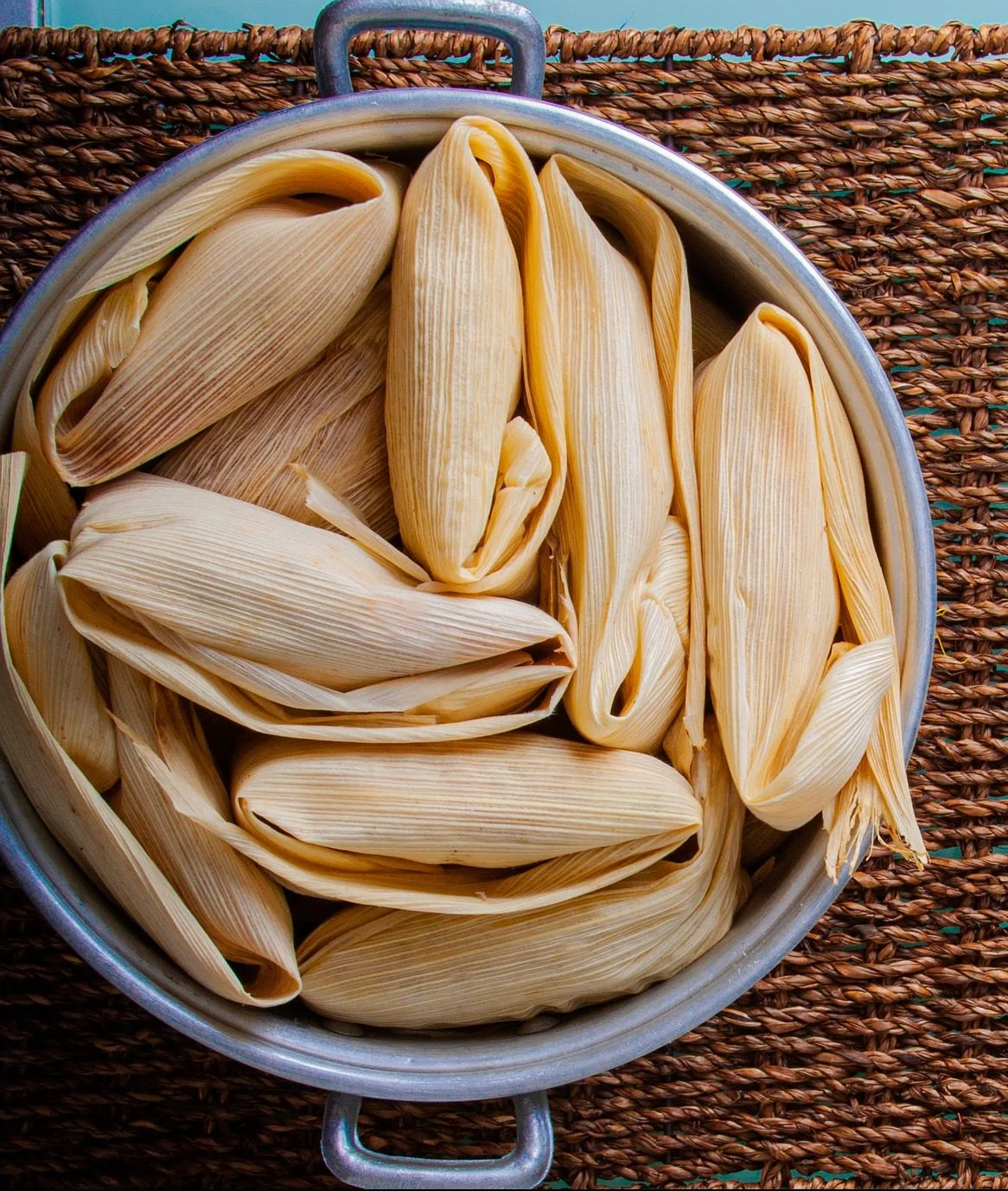 Olla llena de tamales envueltos en hojas de maíz dobladas, sobre un petate.