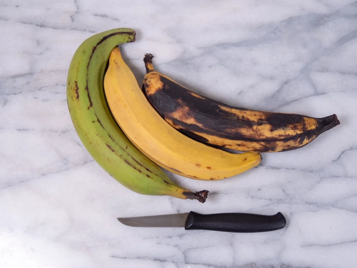 A green plantain next to a ripe yellow plantain, showing the color difference that tells you it is ready