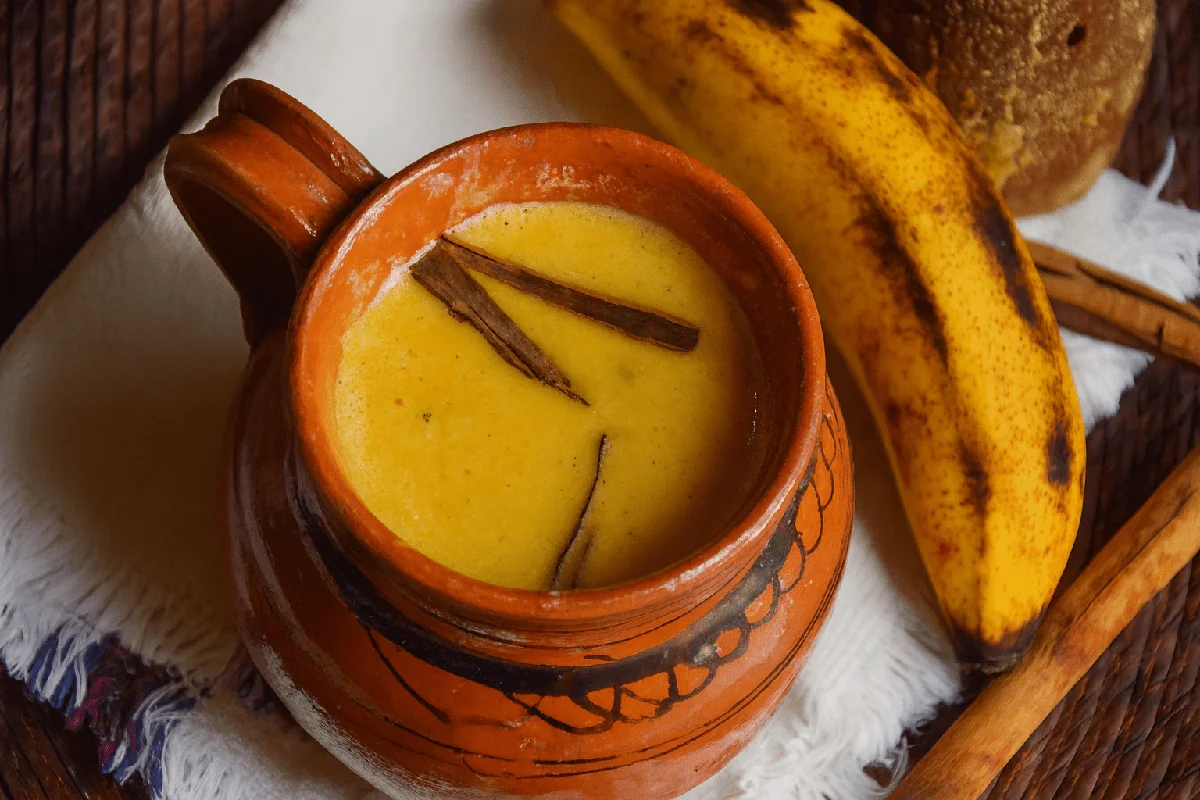 Atol de plátano served warm in a clay mug with cinnamon, beside a ripe plantain