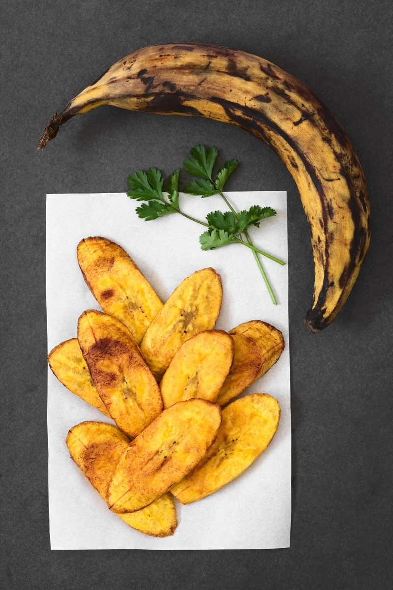 A ripe black-spotted plantain next to fried platanitos, showing how ripe a plantain should be