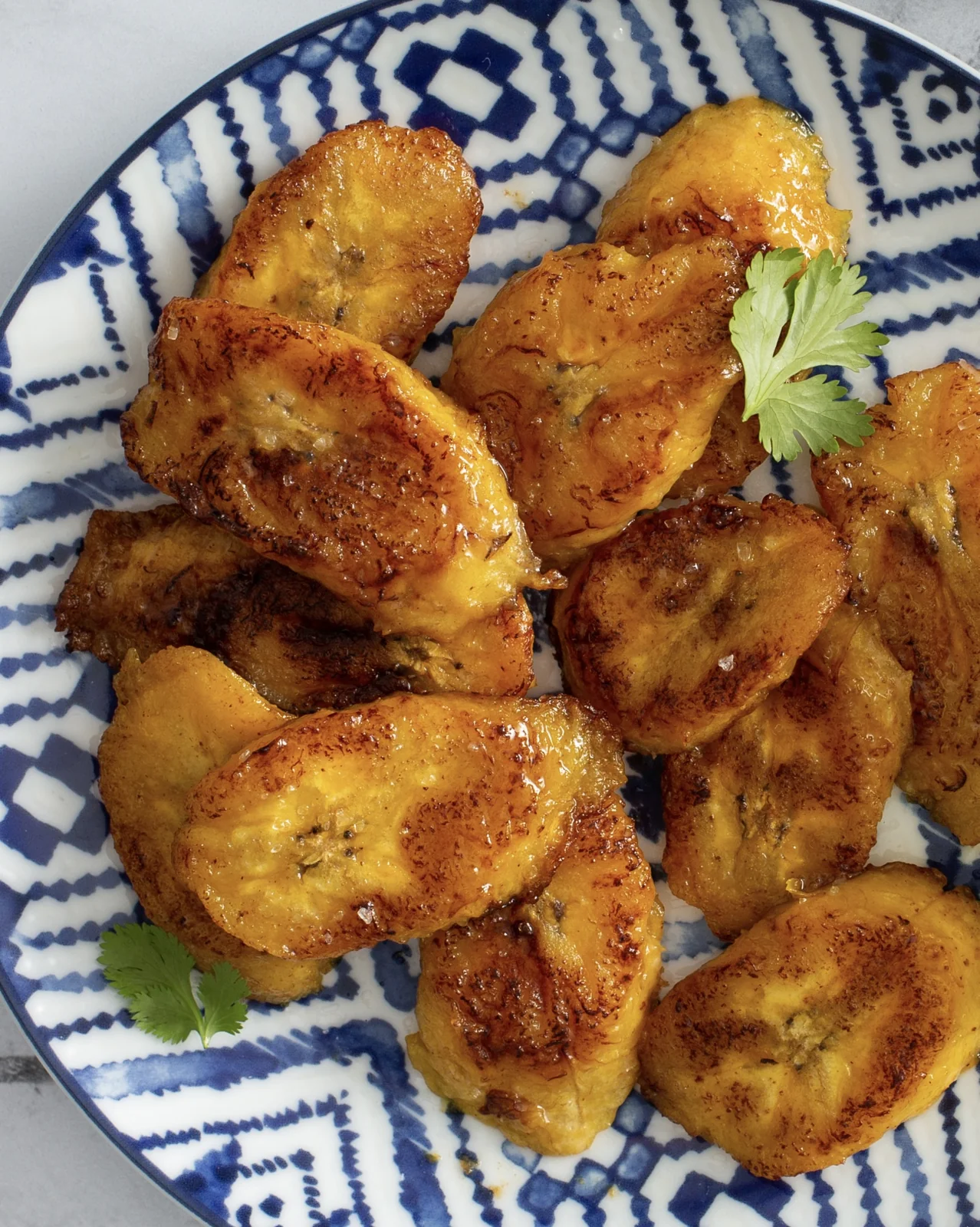 Guatemalan platanitos fritos, caramelized ripe plantains served on a blue patterned plate with cilantro