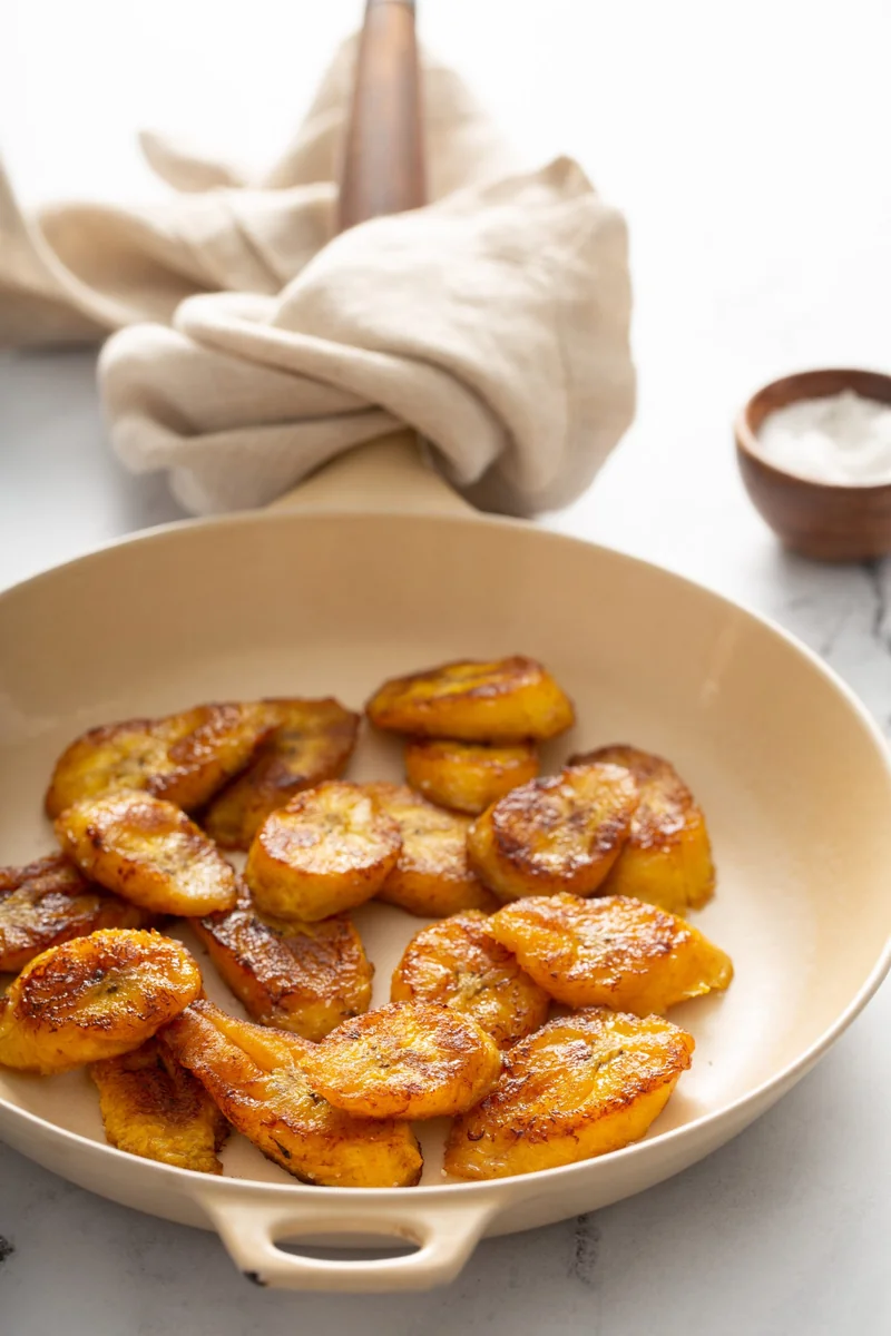 Platanitos fritos frying in a skillet, turning golden on both sides