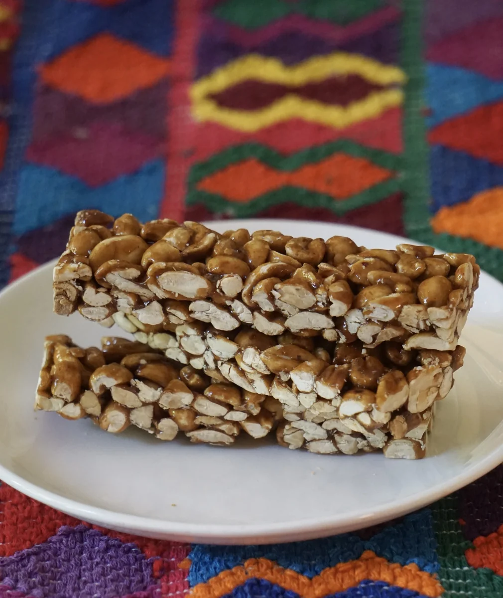Dos barras de maní, maní tostado unido con azúcar caramelizada, apiladas en un plato blanco sobre tela típica