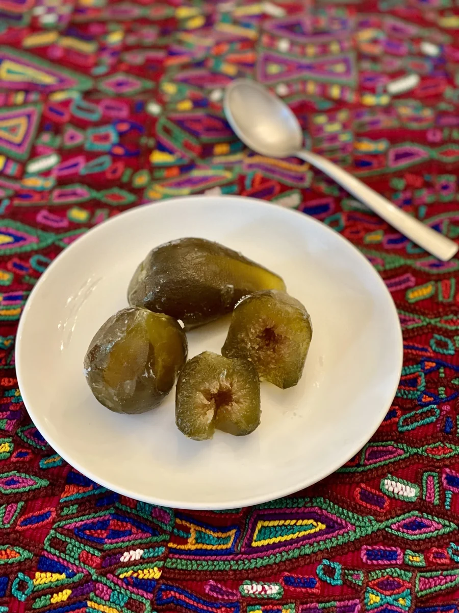 Higos cristalizados en plato blanco sobre tela típica, uno partido mostrando el centro rojo