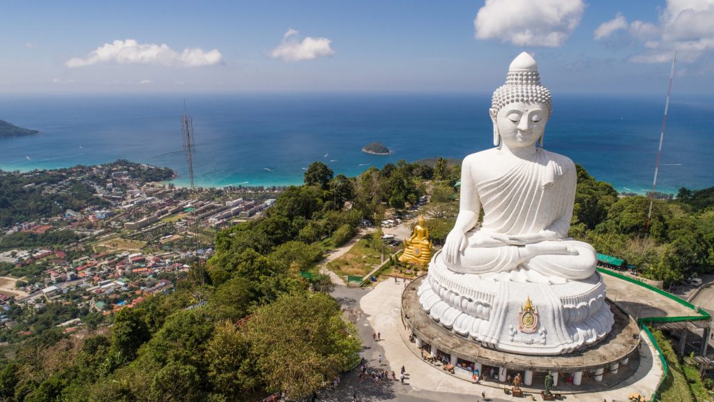 Large white Buddha statue on a mountain overlooking the city and coastline of Phuket, Thailand.