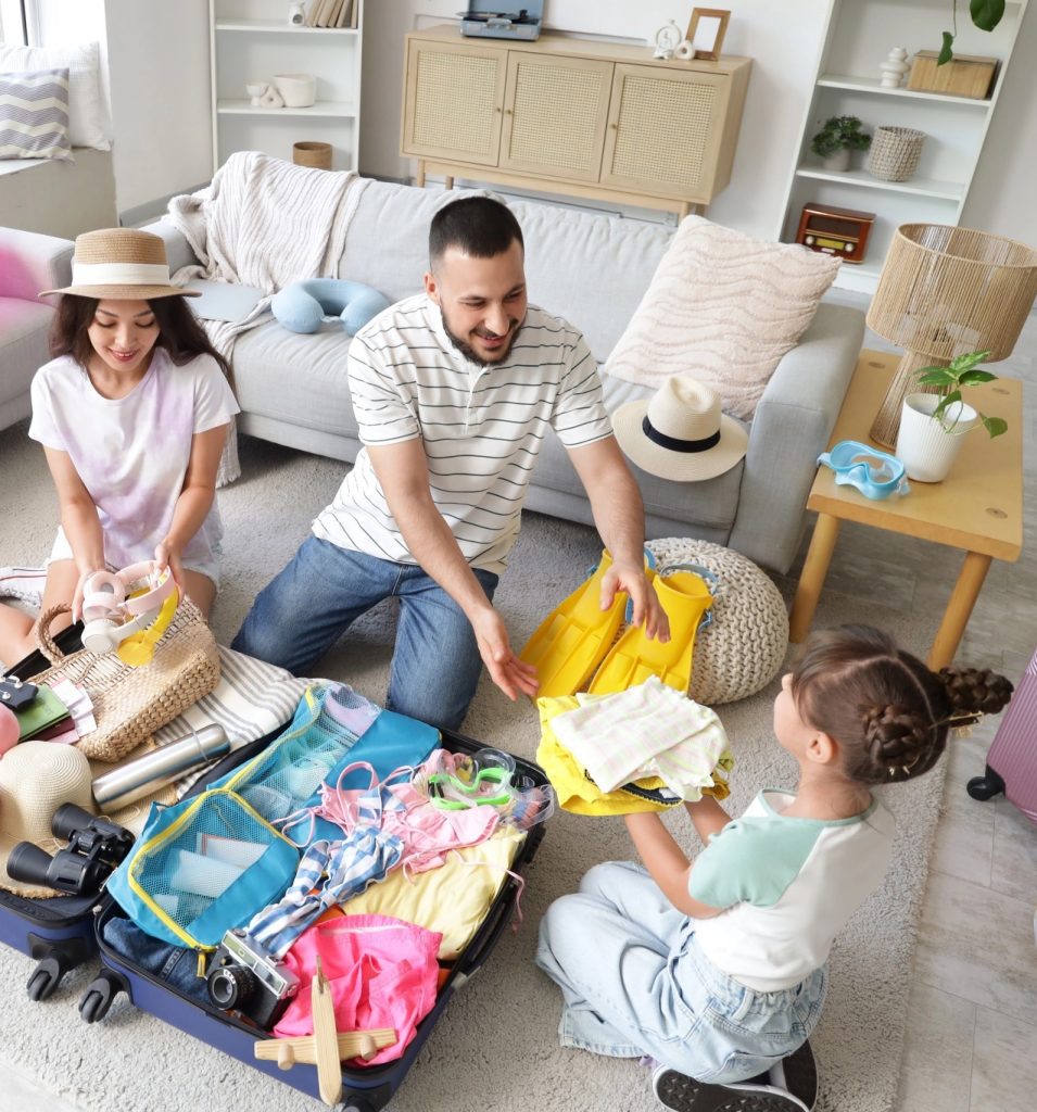 Family with a child packing suitcases for a tropical vacation, surrounded by beach gear like floaties, hats, and snorkeling fins.