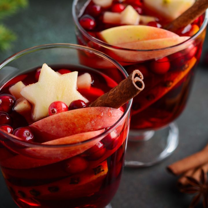 Holiday mulled wine with cranberries, cinnamon, and orange slices in glass mugs
