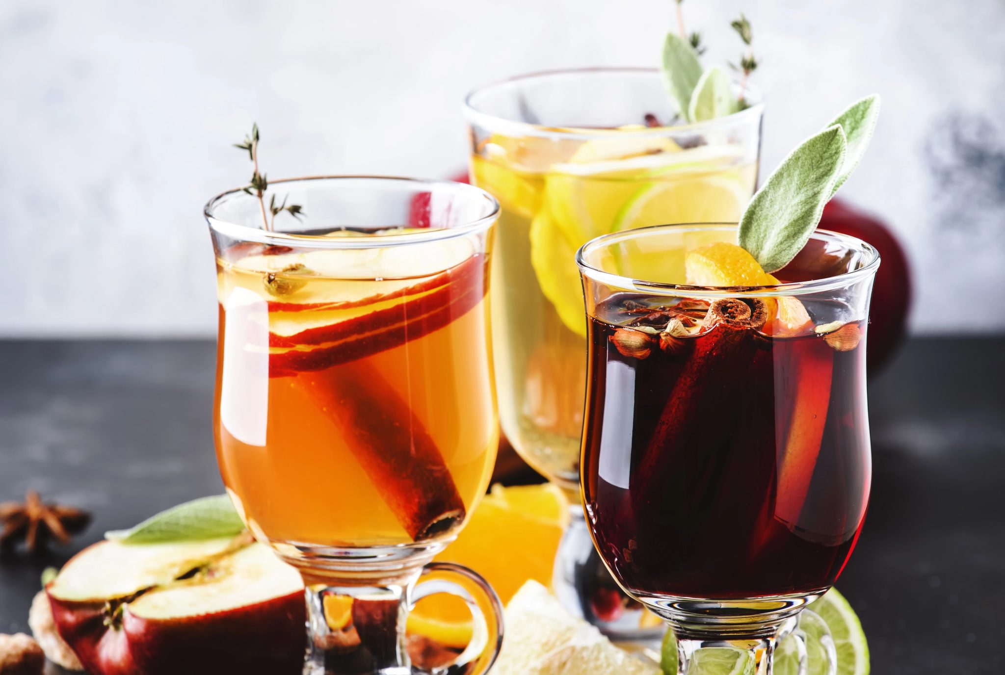 Assorted winter cocktails served warm in glass mugs with citrus slices, cinnamon sticks, and fresh herbs