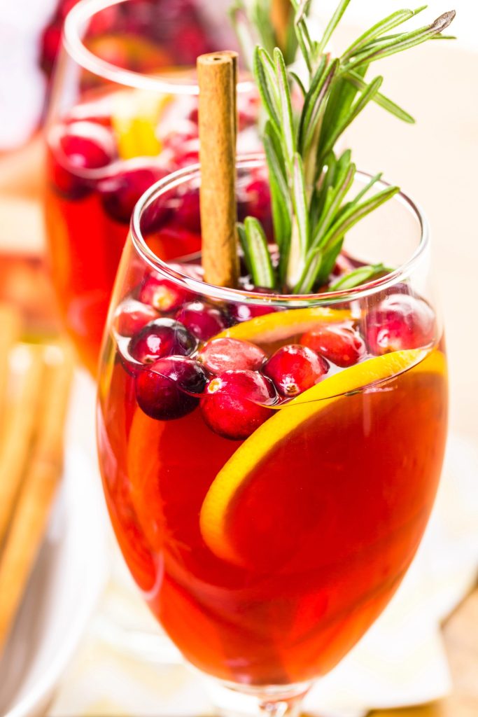 Glass of cranberry sangria garnished with rosemary and cinnamon stick