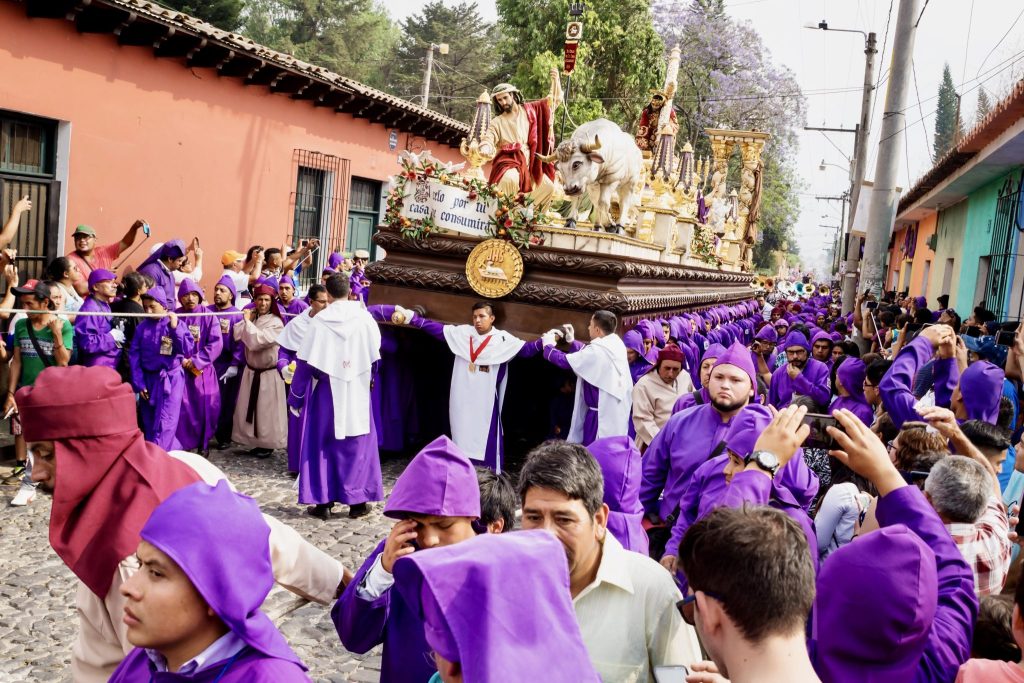 Guatemala Lent processions — the anda of Jesús Nazareno de la Caída with its Temple Cleansing scene, white bull, and golden menorah moves through thousands of purple cucuruchos in Antigua. Discover every Cuaresma procession worth seeing in Guatemala 2026.