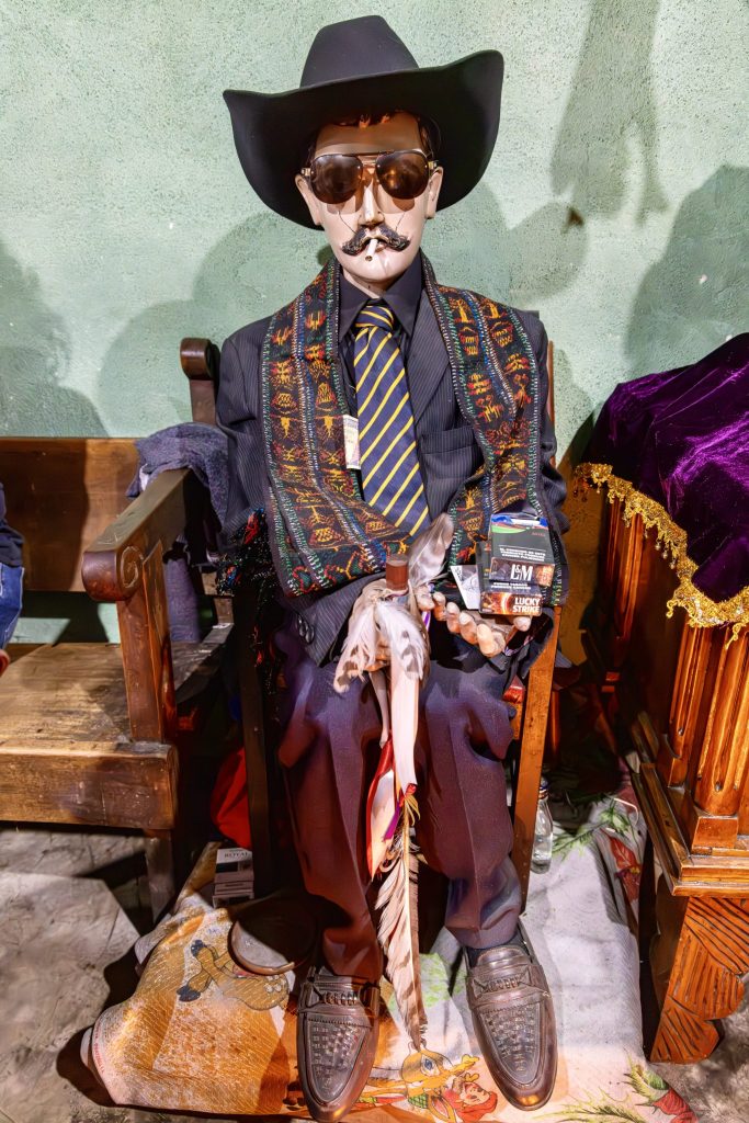 The San Simón figure in a dark suit, tie, sunglasses, and black hat with cigarettes as offerings — Maximón San Andrés Itzapa, Guatemala