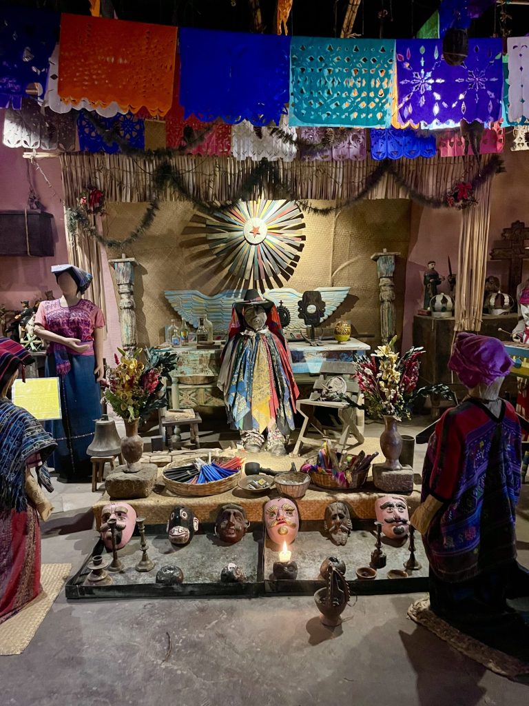 A recreated Maximón altar with ceremonial masks, candles, scarves, and traditional offerings at the Museo de la Música in Finca La Azotea near Antigua, Guatemala