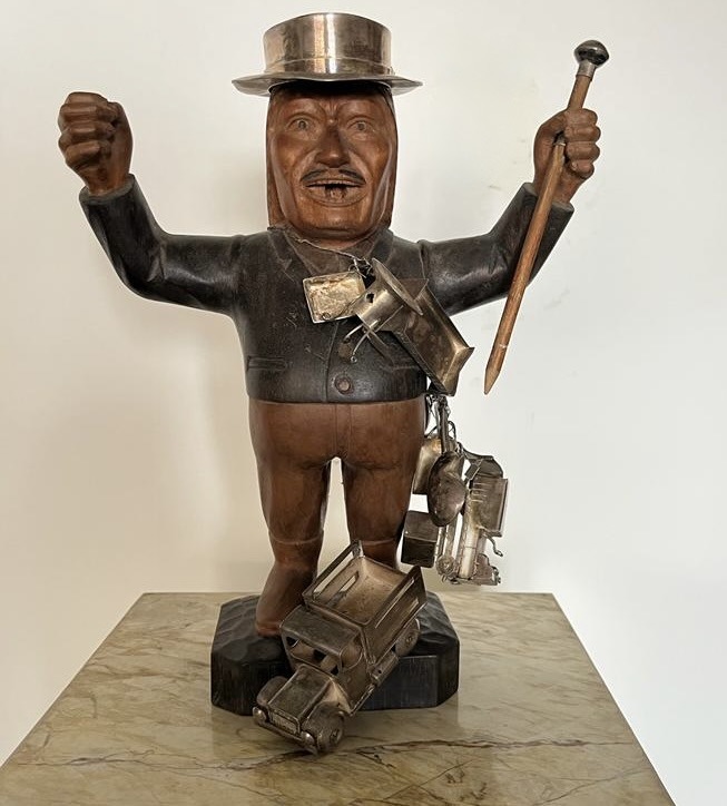 A carved wooden Maximón sculpture with silver milagro offerings including a truck and tools — Guatemalan folk art representation of Maximón, Guatemala