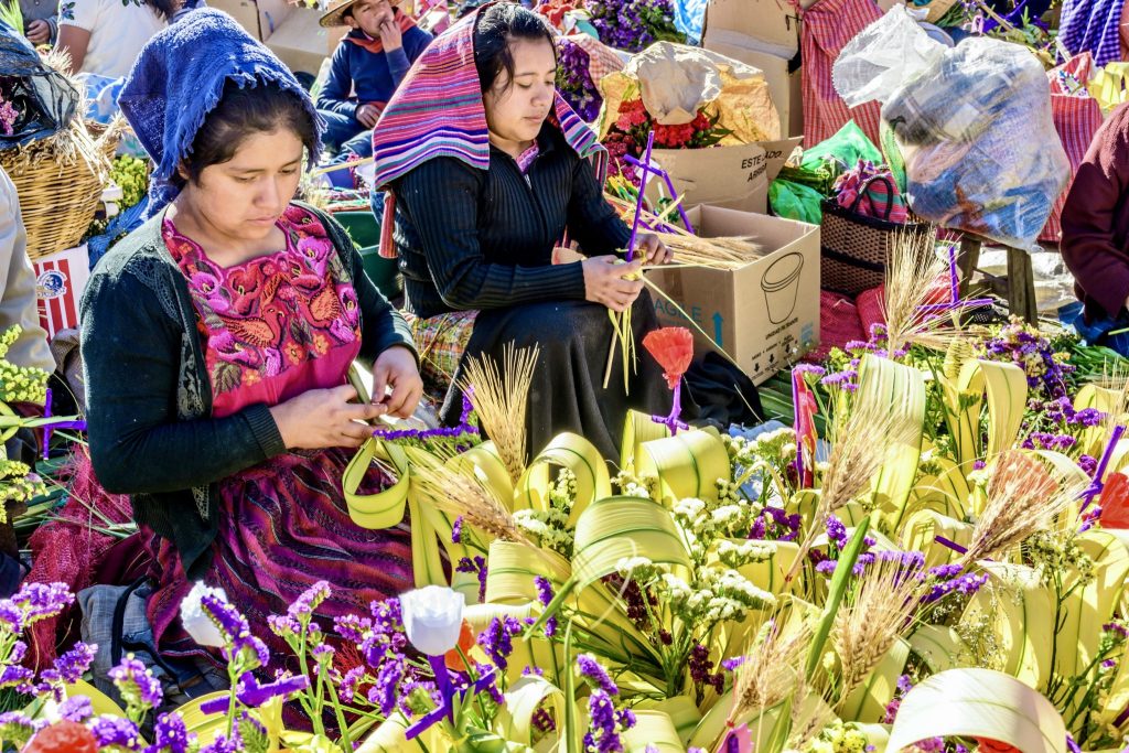 Guatemala Holy Week travel — Maya women in embroidered huipil weave ramos de palma at the Chichicastenango market for Domingo de Ramos. Find out everything to see during Cuaresma and Holy Week in Guatemala 2026.