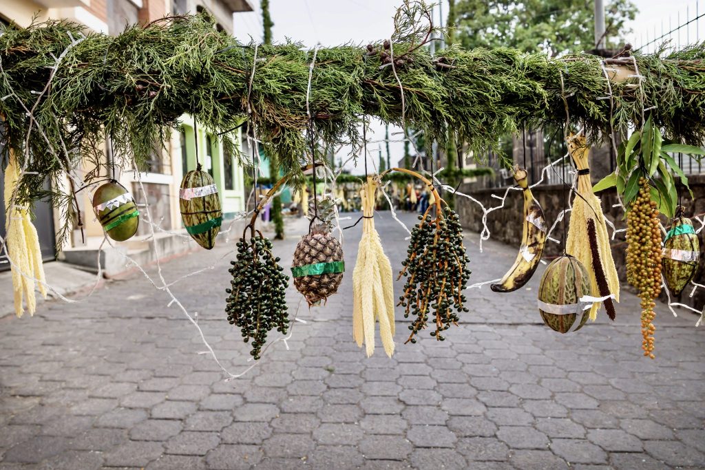 Ceremonial fruit bower hung with pineapples, cacao, and bananas over street — ancient Semana Santa traditions in Santiago Atitlán, Guatemala