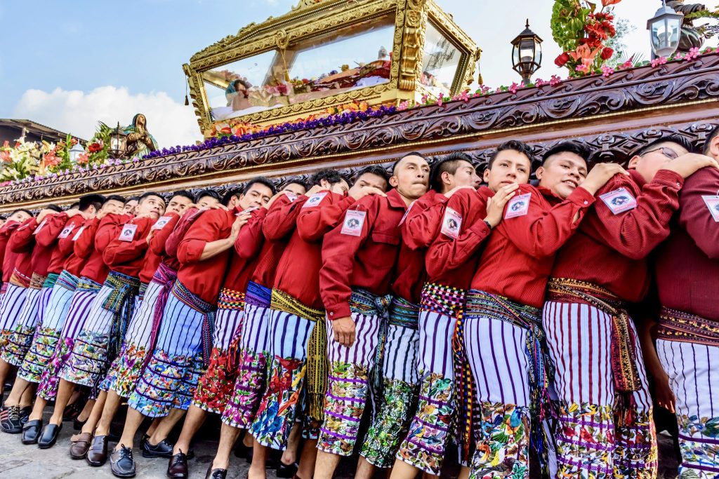 Tz'utujil Maya men in red shirts and traditional embroidered traje carrying the gold-framed anda of the Señor Sepultado during the Good Friday procession — Semana Santa in Santiago Atitlán, Guatemala