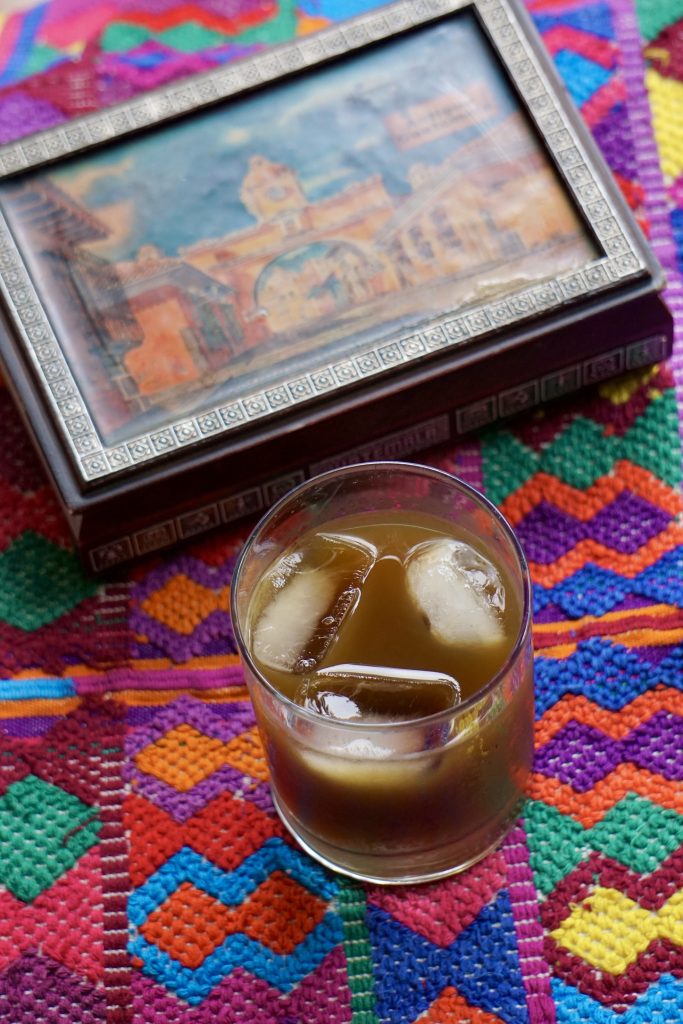 Vaso de fresco de chilacayote con hielo sobre mantel guatemalteco con caja decorativa de Antigua Guatemala al fondo