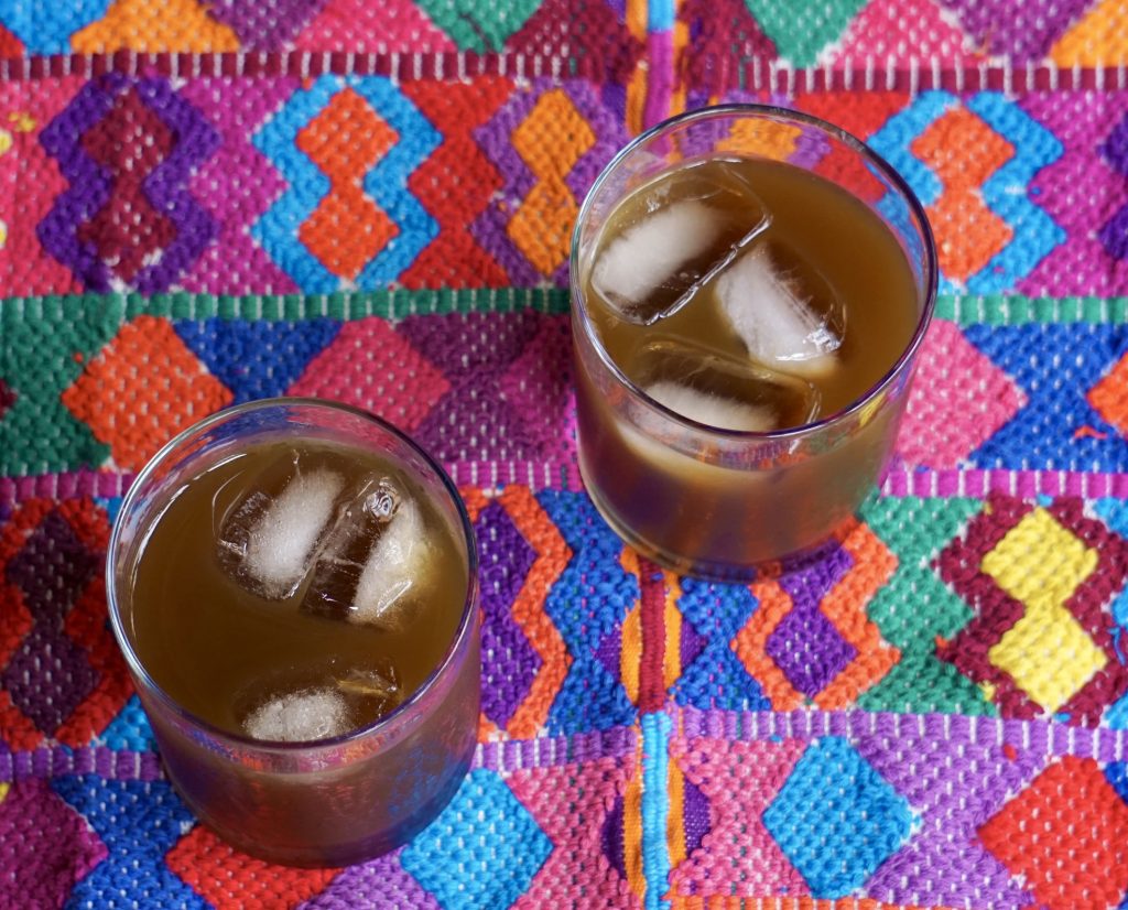 Two glasses of fresco de chilacayote over ice seen from above on a colorful Guatemalan embroidered tablecloth