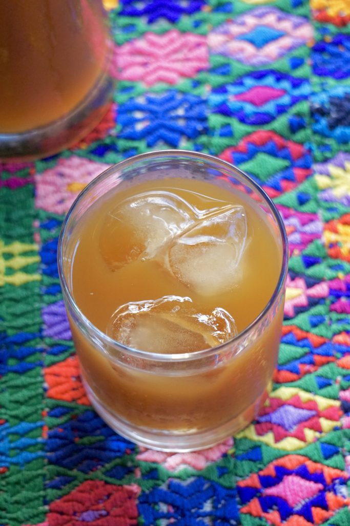 Vista desde arriba de un vaso de fresco de suchiles con hielo sobre un mantel bordado guatemalteco