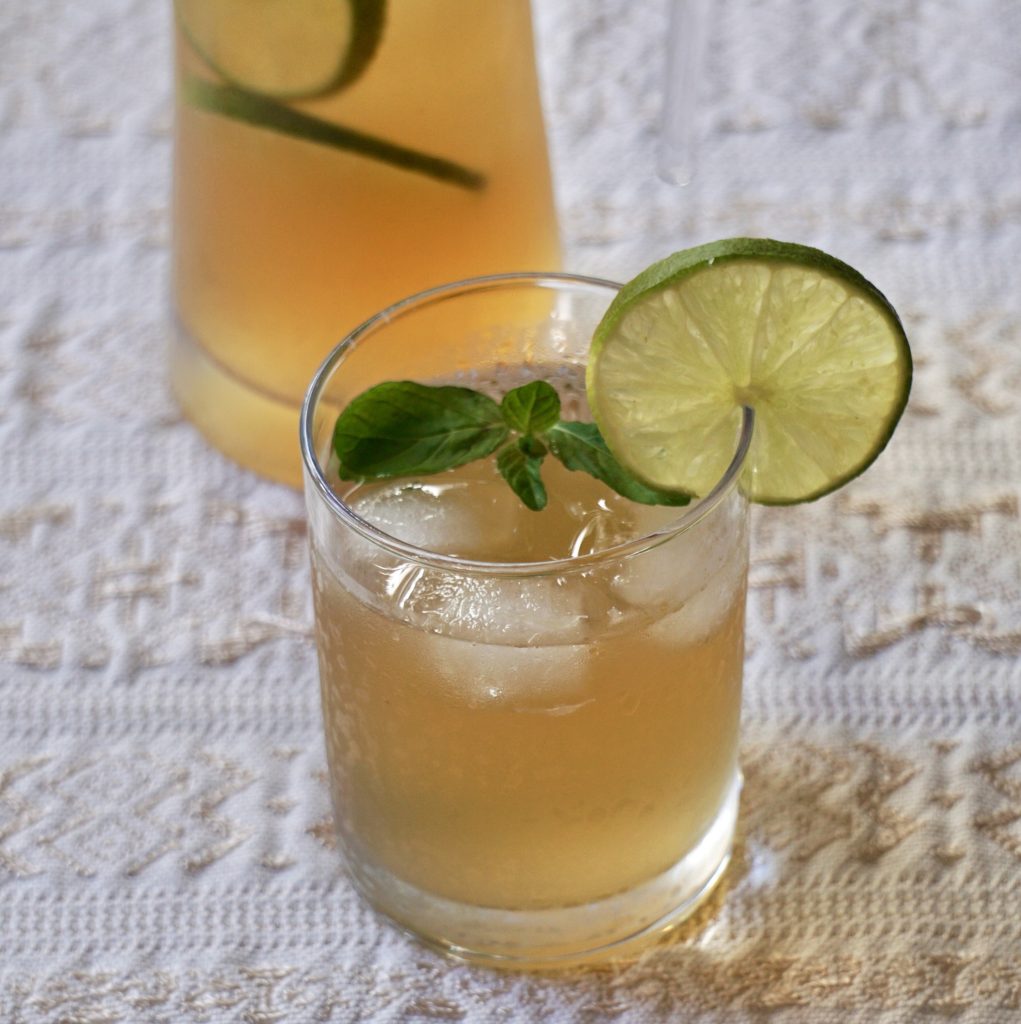 Glass of fresco de chinchivir over ice garnished with a lime slice and fresh mint, with a pitcher in the background on a white tablecloth