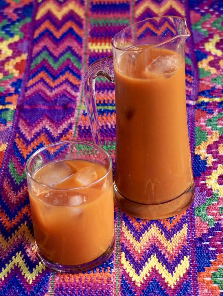 Glass and tall pitcher of fresco de tiste with ice on a bright multicolor Guatemalan embroidered tablecloth