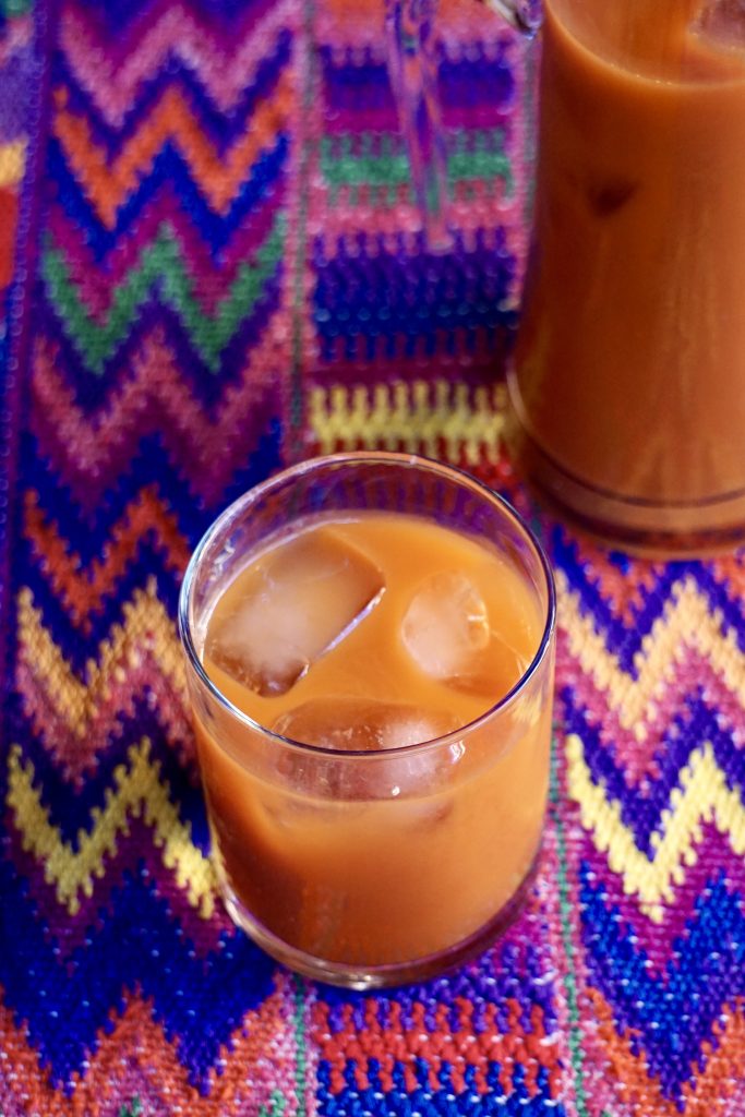 Primer plano de un vaso de fresco de tiste con hielo sobre mantel guatemalteco multicolor con una jarra al fondo