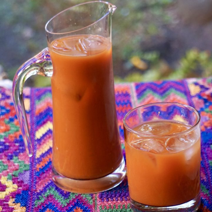 Pitcher and glass of fresco de tiste over ice on a colorful Guatemalan textile with a soft blurred background